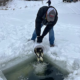 A man stocking a lake with fish from a bucket in the winter.